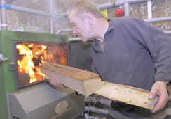 Photograph of a man adding fuel to a log burner taken at Beech Hill, Morchard Bishop