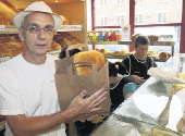 Photograph of a baker with a loaf of bread in a brown paper bag